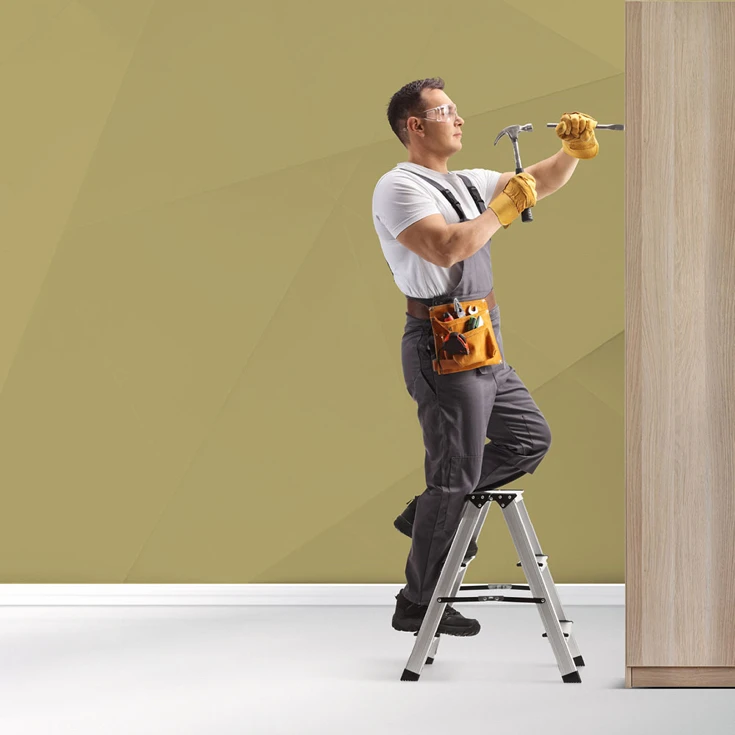 A handyman wearing safety gear and holding a hammer and chisel, working on a wooden surface while standing on a step ladder, symbolising craftsmanship and professionalism, against a blue geometric background.